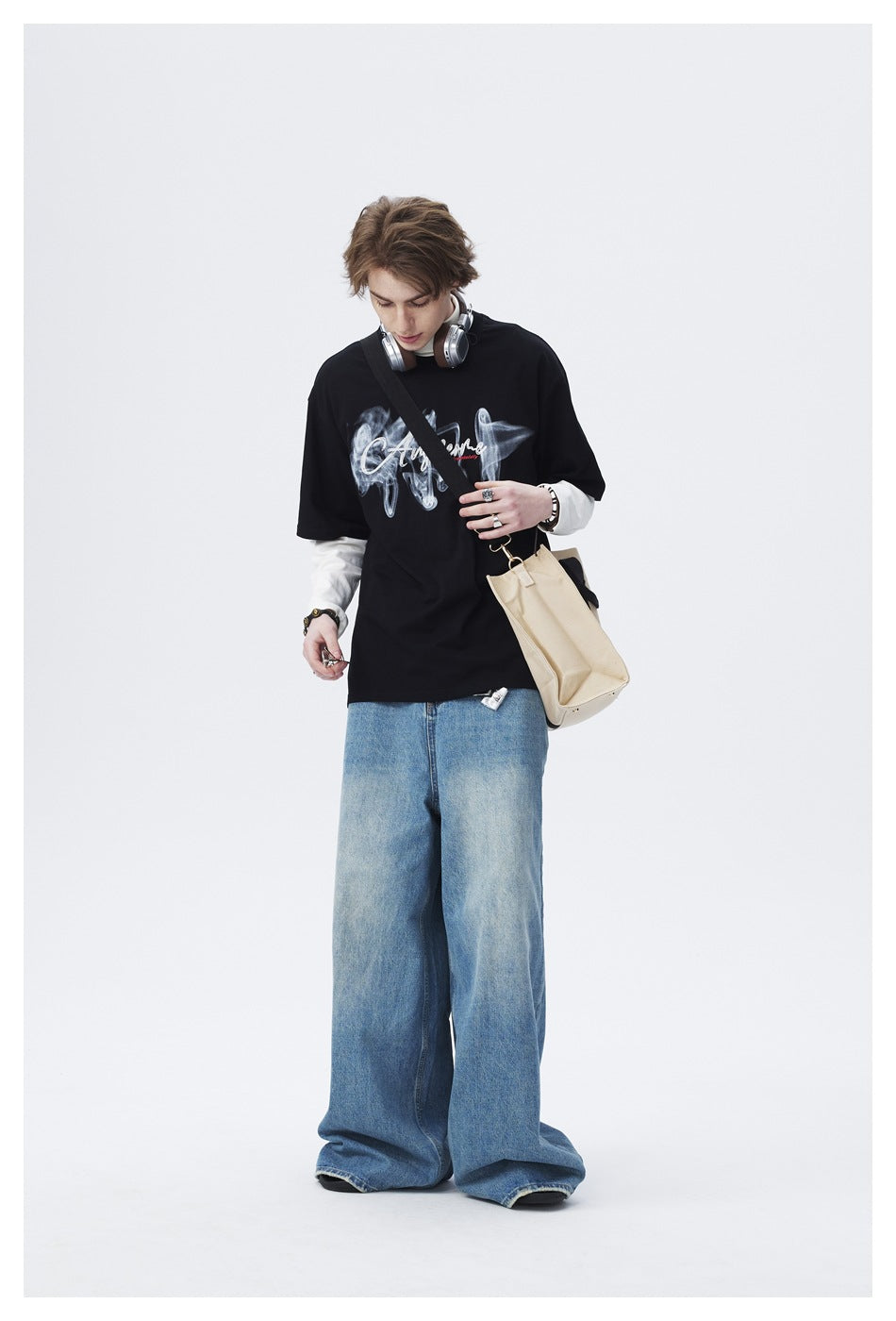 Model wearing a black graphic T-shirt over white long sleeves with loose light-blue jeans.