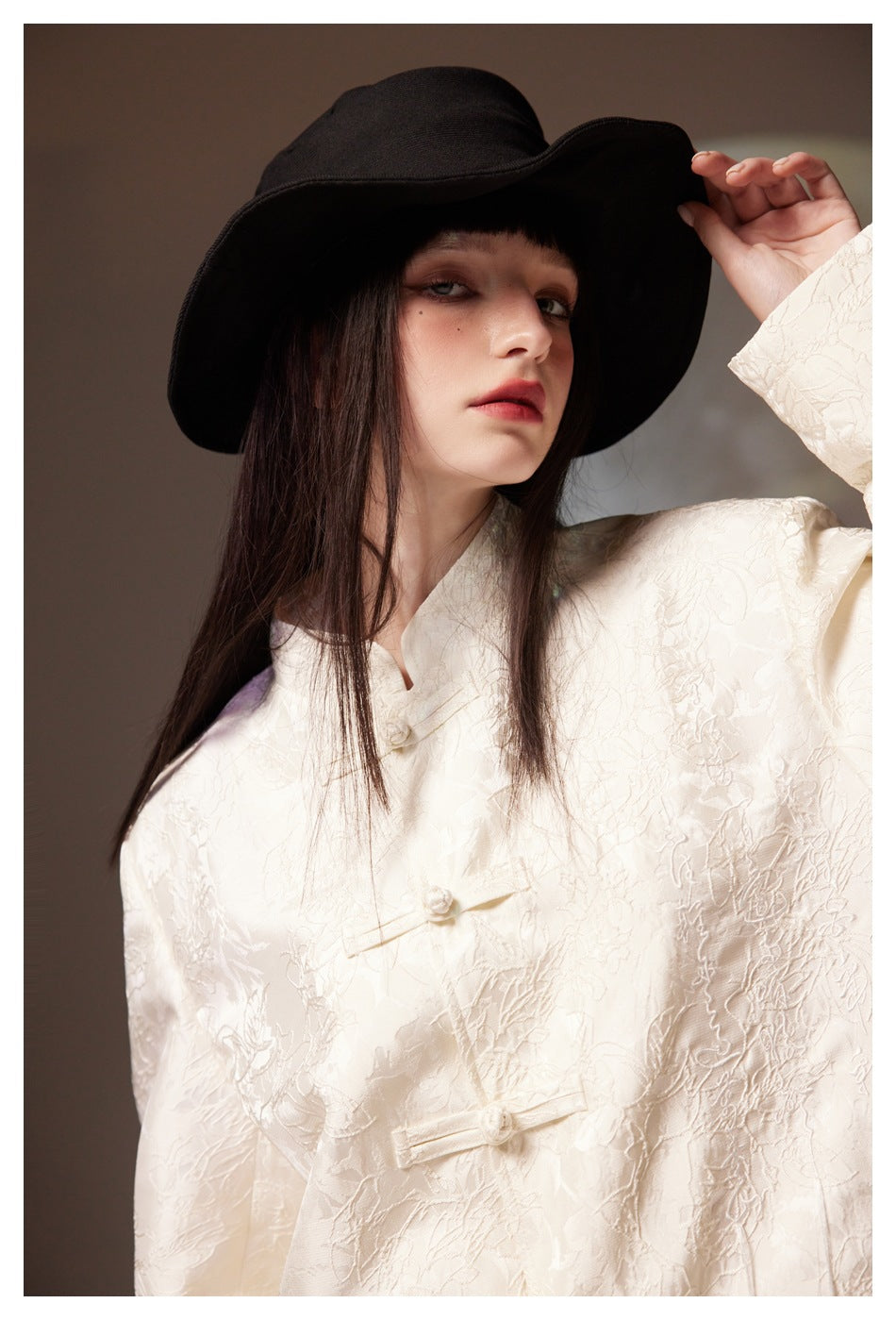 Close-up of the ivory jacket's raised floral texture and decorative frog closures, worn by a model.