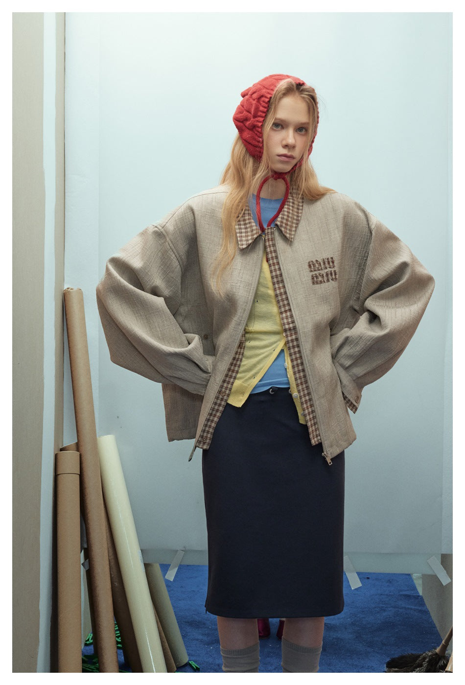 Front view of a model in an oversized taupe jacket with checked trim and chest embroidery, layered over colorful tops.