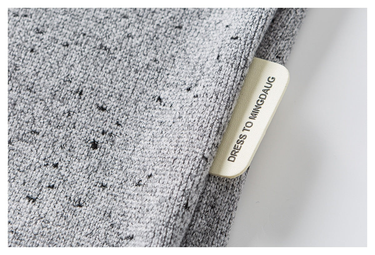 Close-up of a gray flecked knit sweater with a cream-colored side label bearing English text.