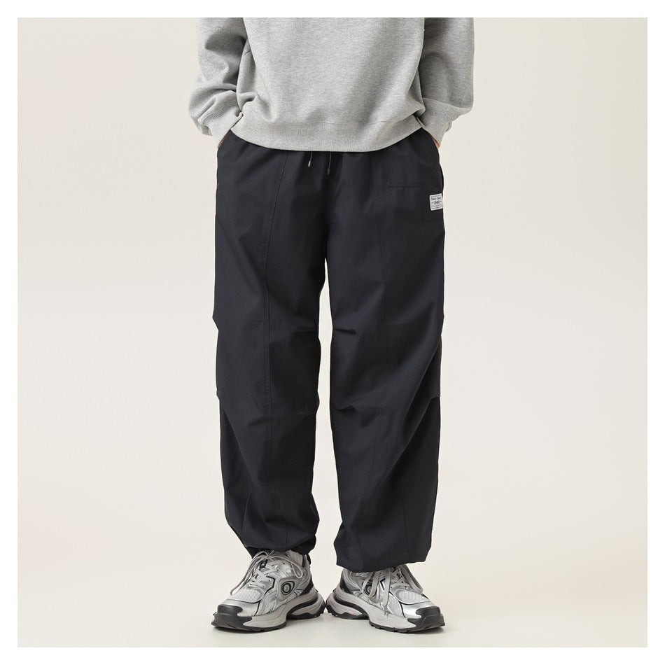 Front view of a model wearing loose black pants with a drawstring waist and panel seams.