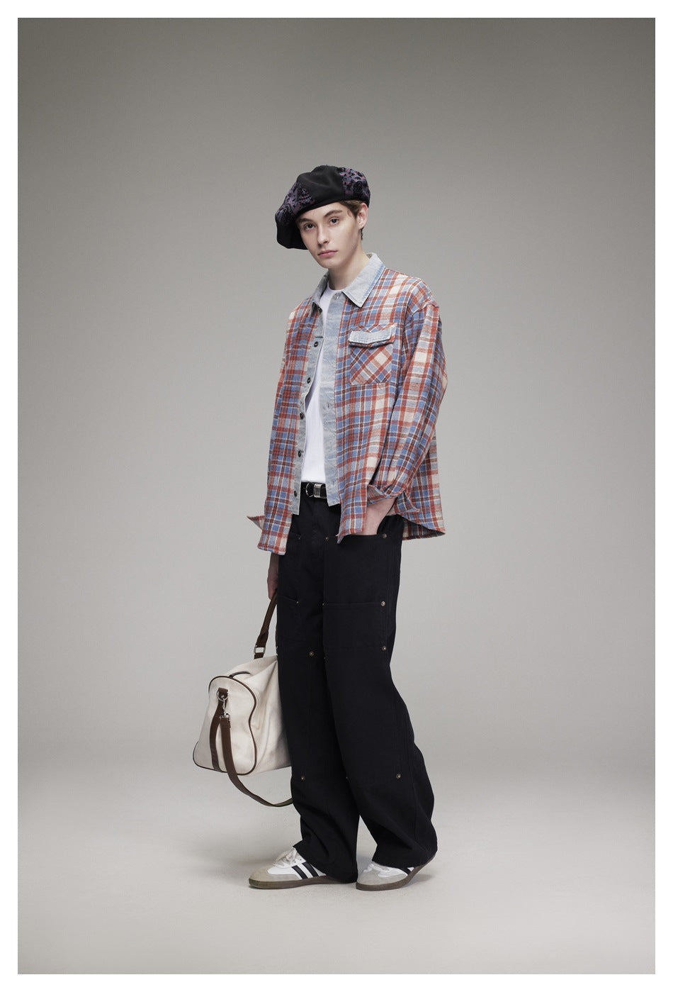 Model wearing a rust, blue and cream plaid button-up shirt with a light denim collar, black trousers and a patterned beret.
