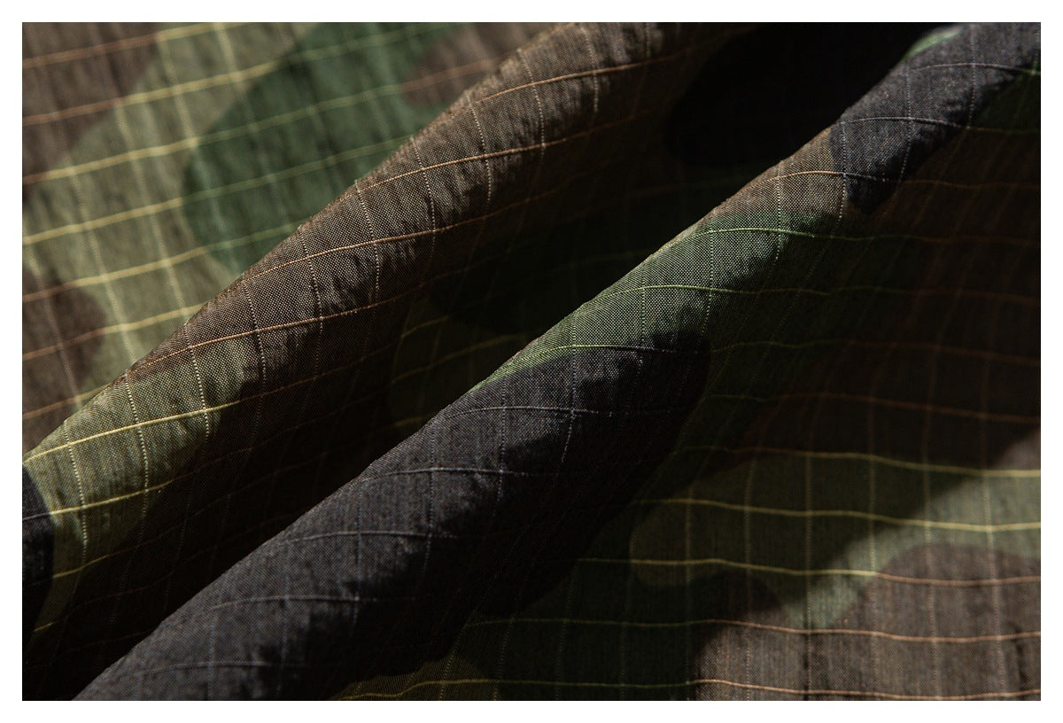 Macro view of green, brown, and black camouflage fabric with fine grid lines and folded seams.