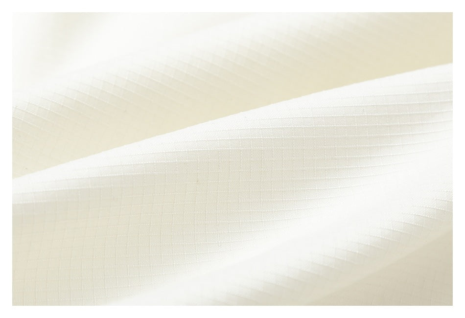 Extreme close-up of ivory fabric showing its fine grid-like texture and stitched edge.