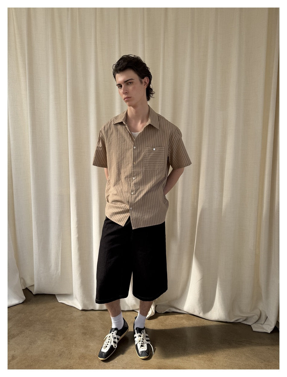 Model wearing a taupe striped short-sleeve button-up shirt with a chest pocket, black shorts, and sneakers.