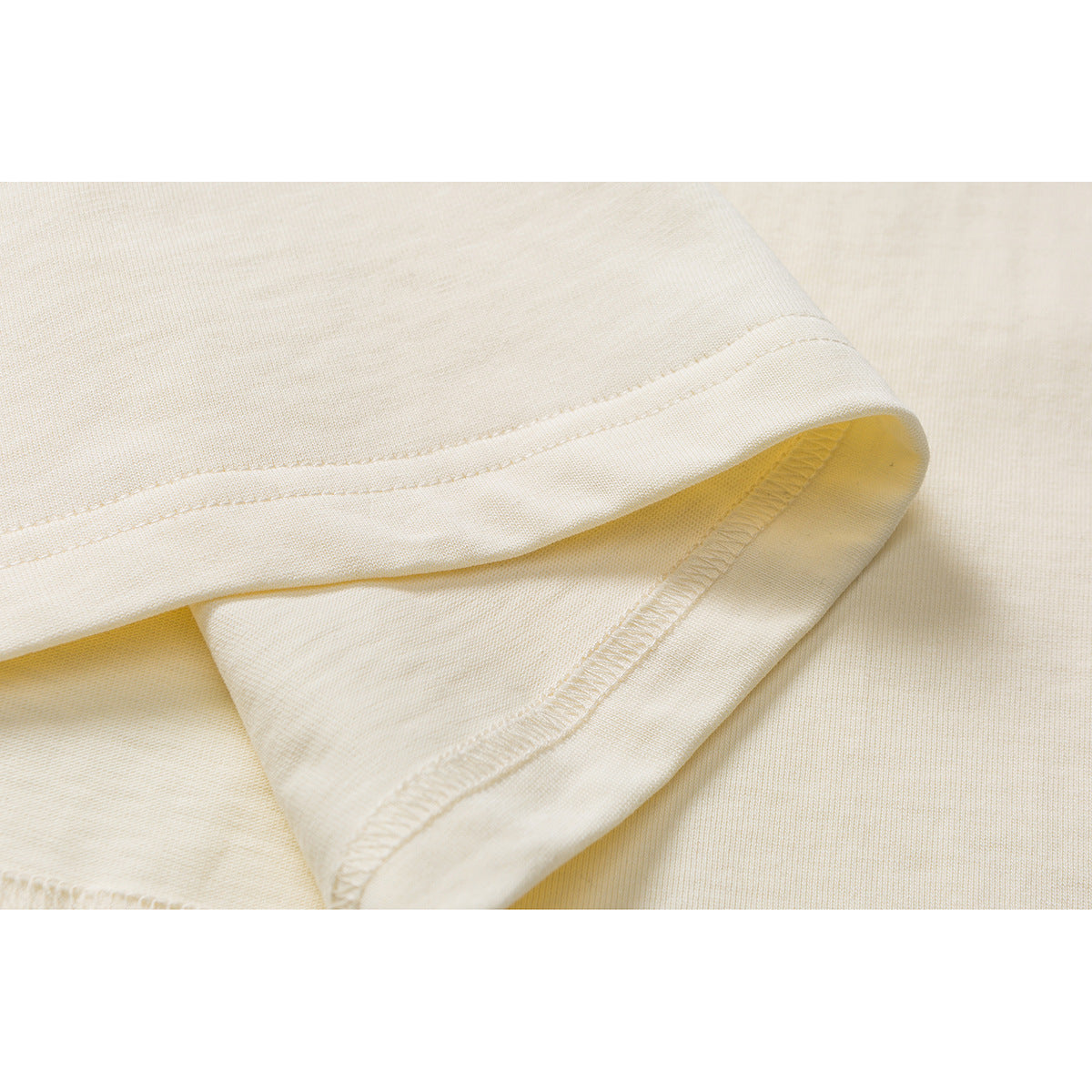 Close-up of the ivory T-shirt’s folded hem, showing the stitching and inside seam.