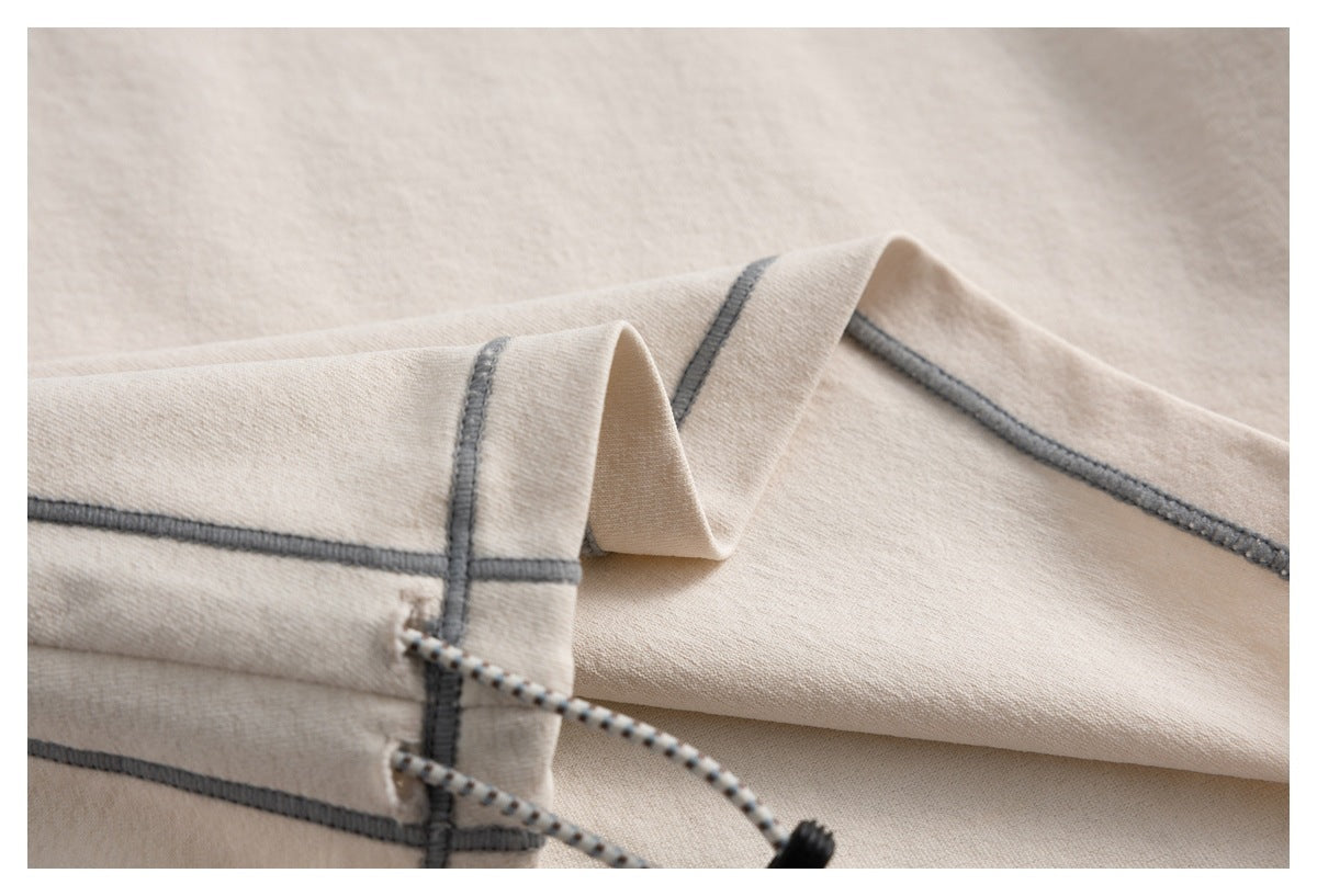 Close-up of beige garment panels with dark gray overlock seams and a cord emerging near the edge.