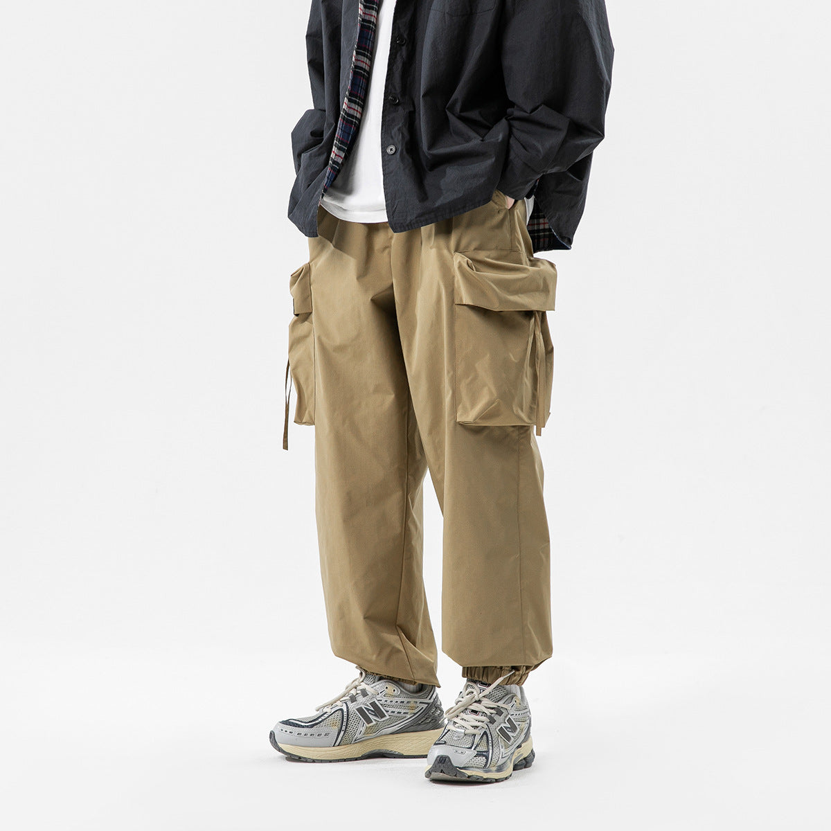 Model wearing loose tan cargo pants with large flap pockets and elastic cuffs, shown from the front.