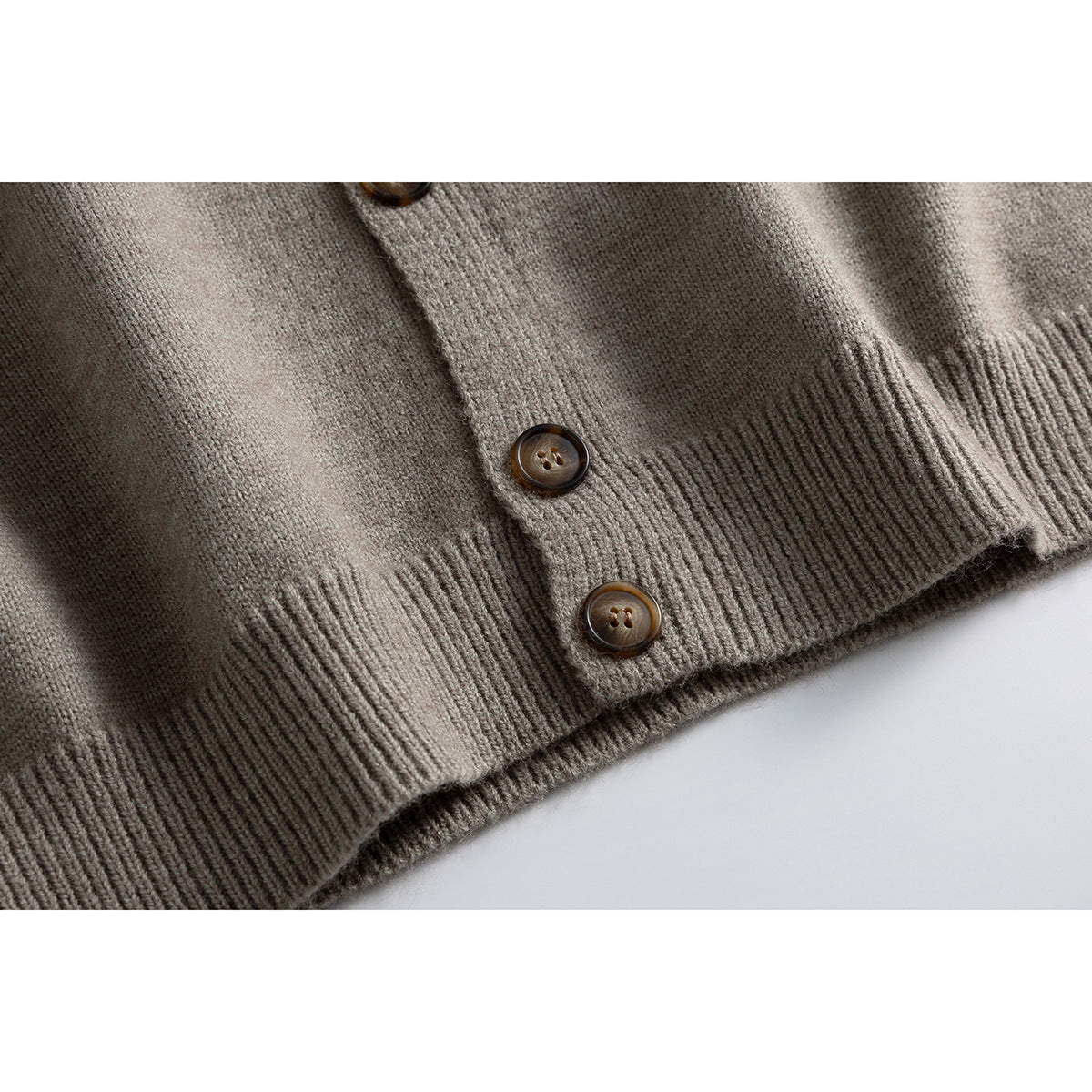 Close-up of the taupe cardigan's ribbed hem and brown buttons on a pale background.