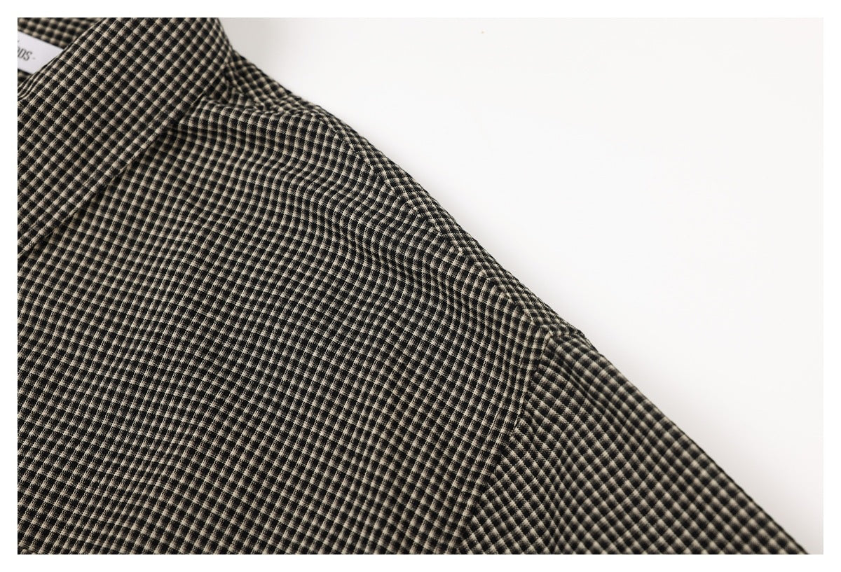 Close-up of black and beige small-check garment fabric, with a partial white label at the upper left.