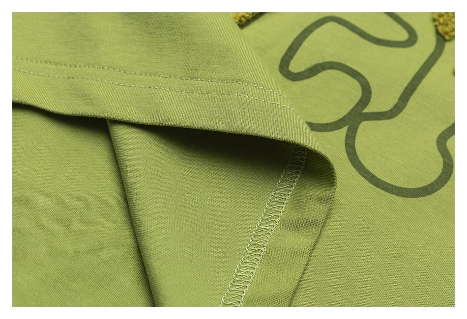 Close-up of a lime-green garment hem with stitching, an overlocked seam, and part of a dark graphic print.