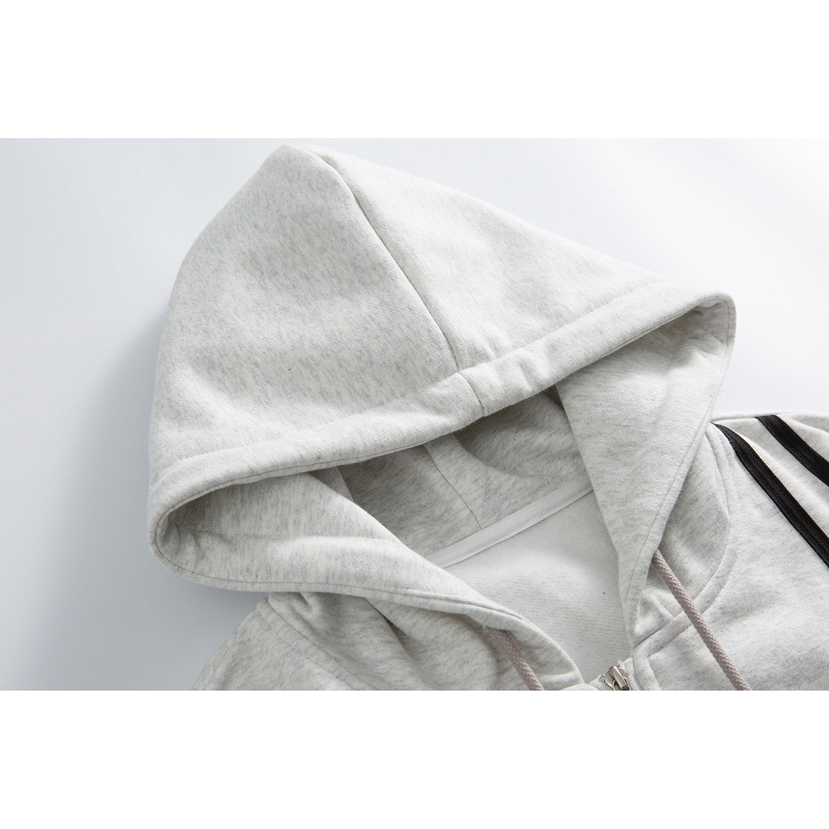 Close-up of a light gray marl hoodie showing the lined hood, drawstrings, zipper, and black shoulder stripes.