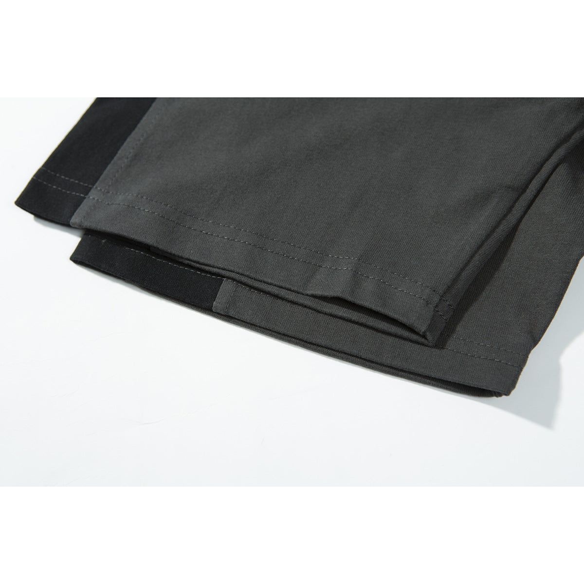 Close-up of the double-stitched hem on a charcoal and black color-block T-shirt.