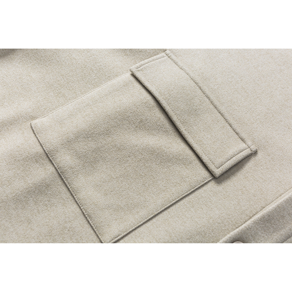 Close-up of a beige-gray shirt jacket’s large rectangular pocket with a long overlapping flap.