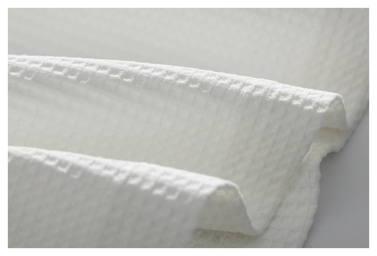 Close-up of white textured fabric folded to show its raised pattern and soft-looking surface.