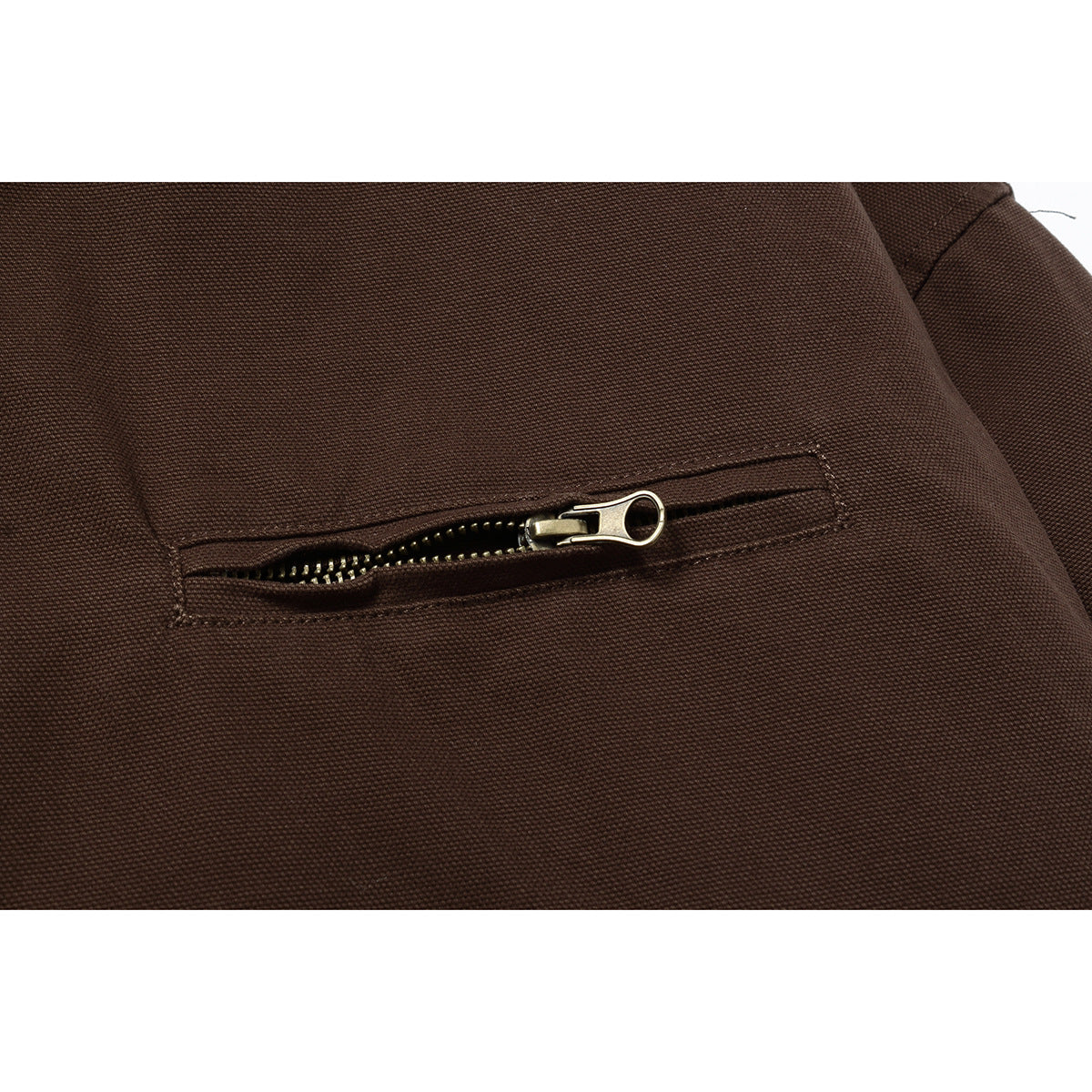 Close-up of a dark brown jacket's horizontal zip pocket with a brass-colored zipper pull.