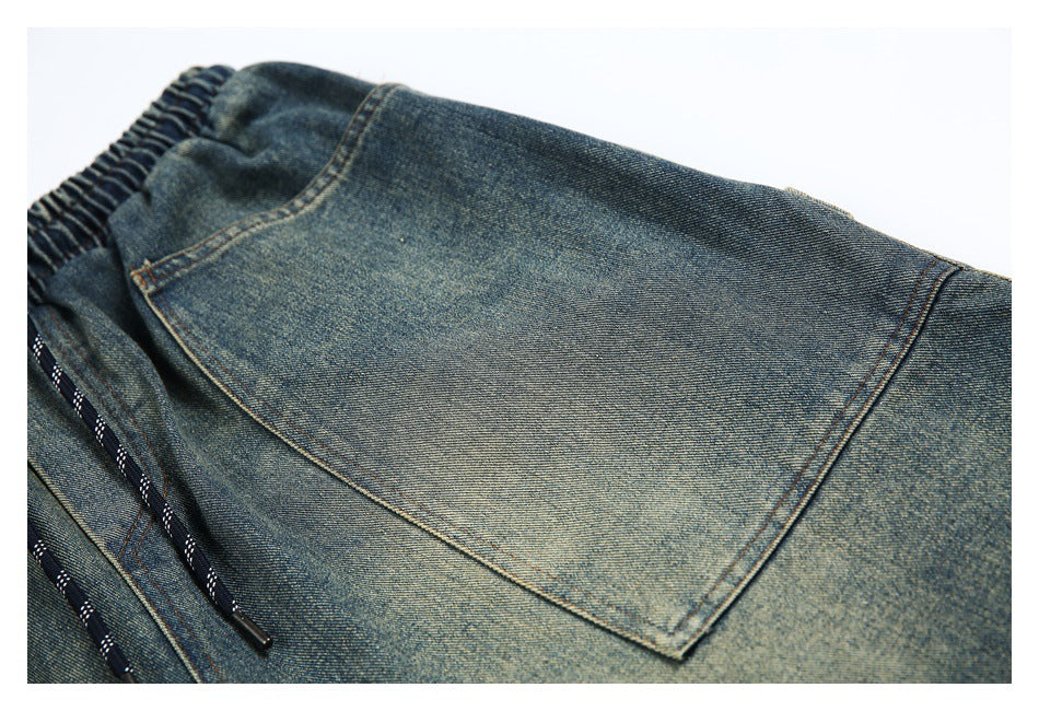Close-up of a large stitched patch pocket on faded blue denim shorts, with part of the drawcord visible.