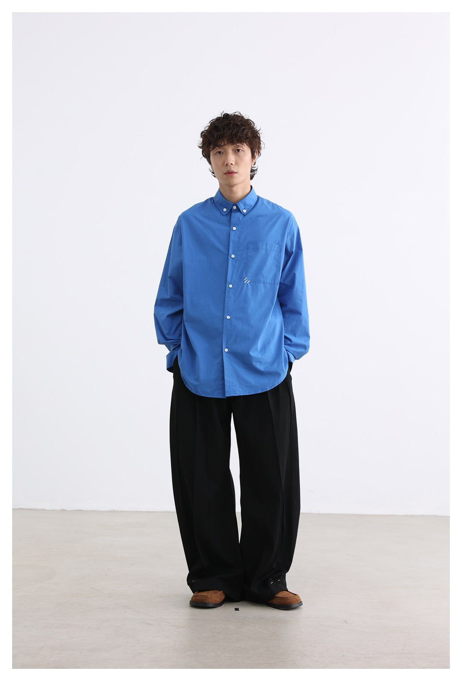 Full-length model wearing a bright blue button-down shirt with black wide-leg trousers.