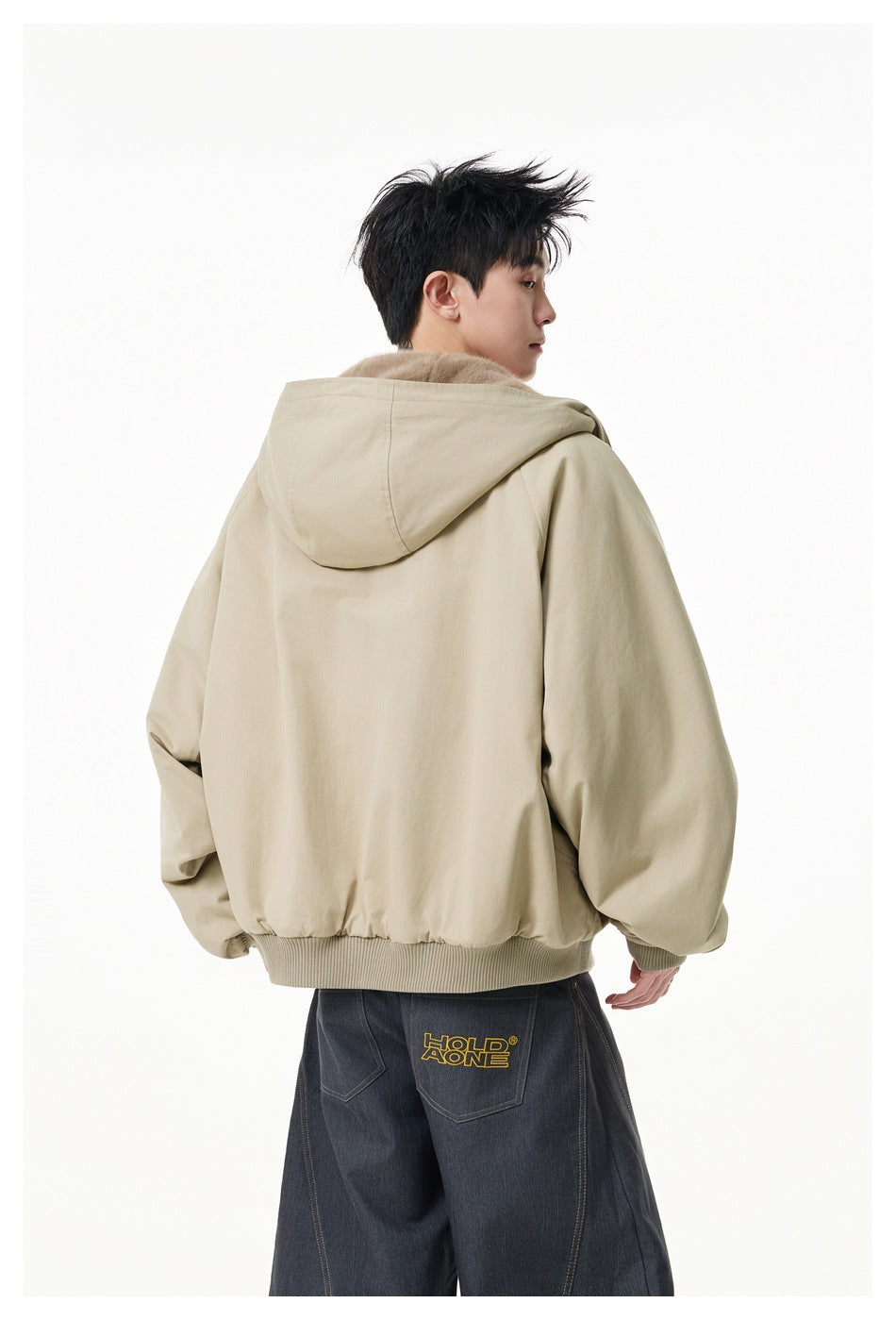 Rear view of a model wearing a beige hooded jacket with ribbed hem and cuffs; yellow lettering appears on his pants.