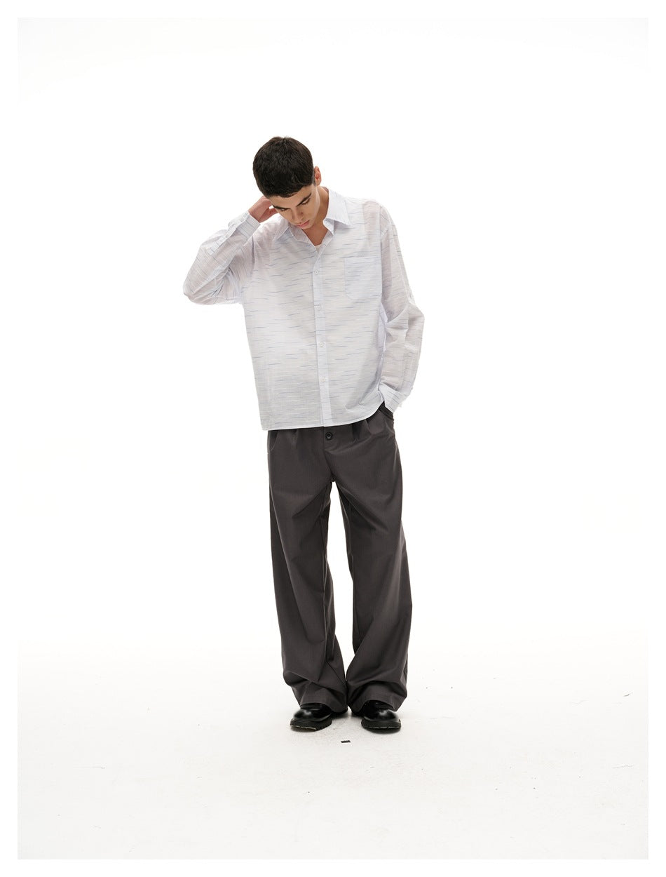 Full-length model wearing a white fine-dash shirt with a chest pocket, loose charcoal trousers and black shoes.