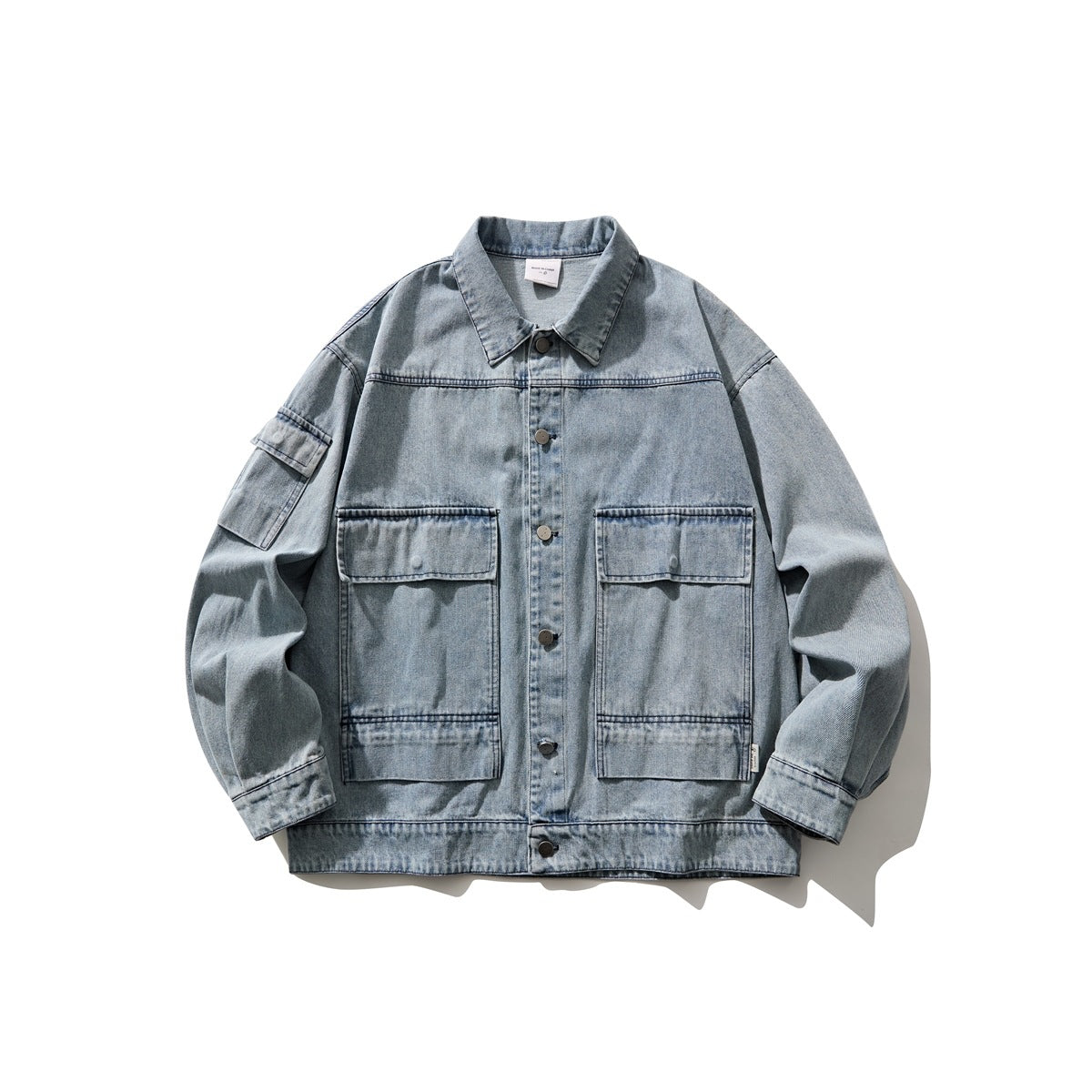Light blue washed denim jacket flat lay with large flap chest pockets, snap buttons and sleeve pocket
