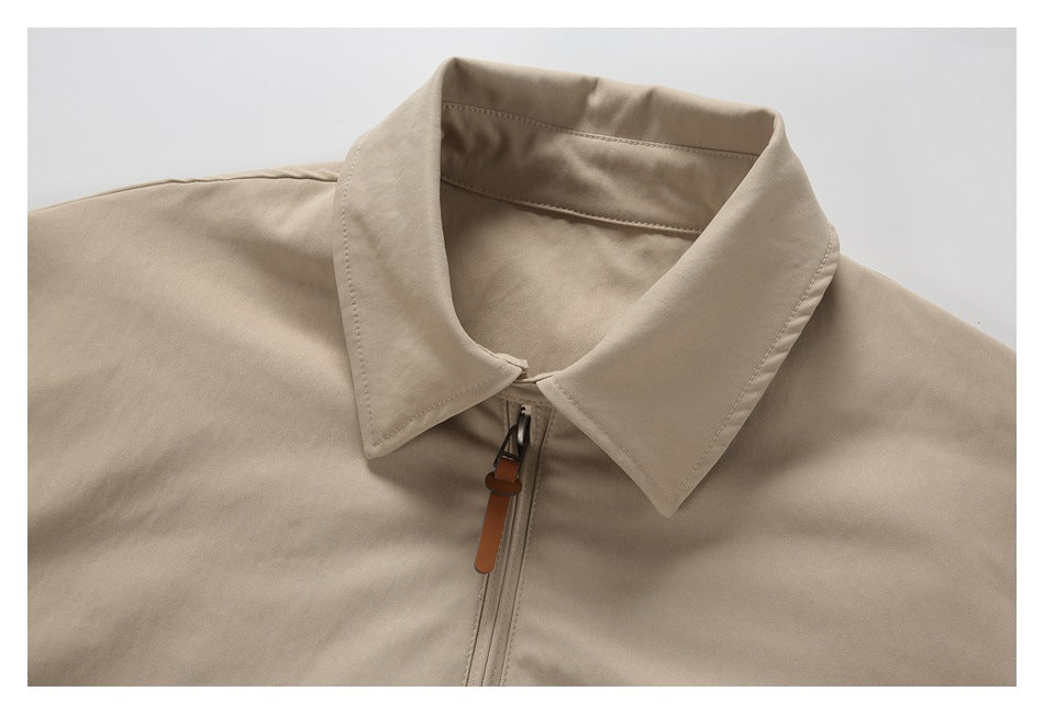Close-up of a beige jacket's pointed collar and front zipper with a brown pull tab.