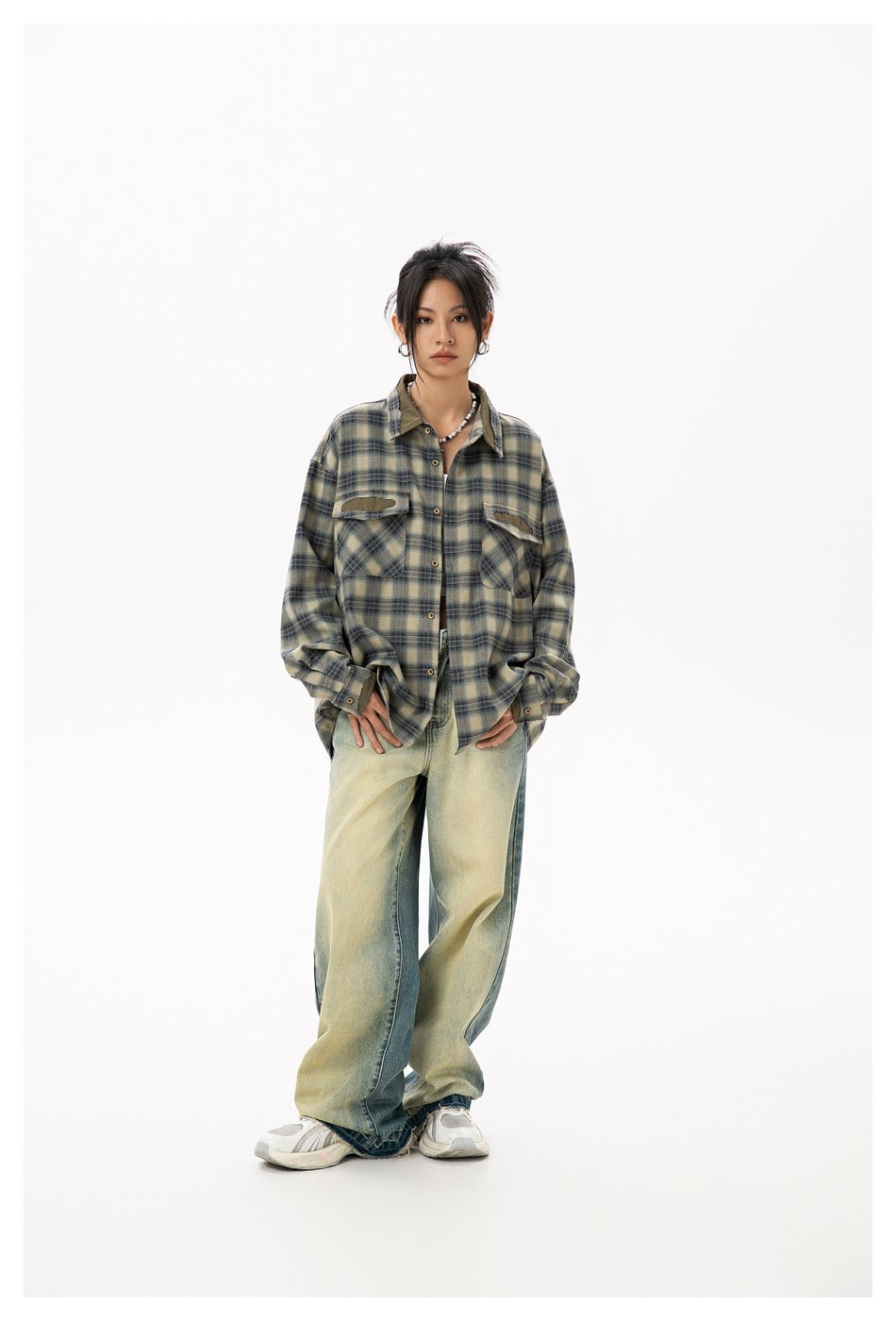 Model wearing open green plaid shirt over a white top with wide-leg faded jeans and white sneakers, front view