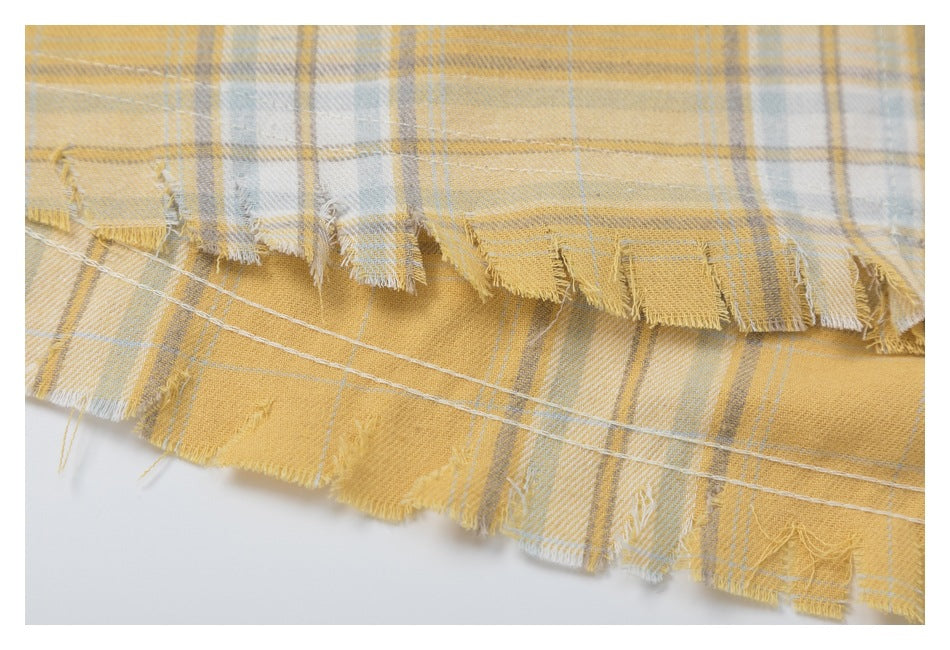 Close-up of layered frayed hems and stitching on mustard yellow plaid fabric.