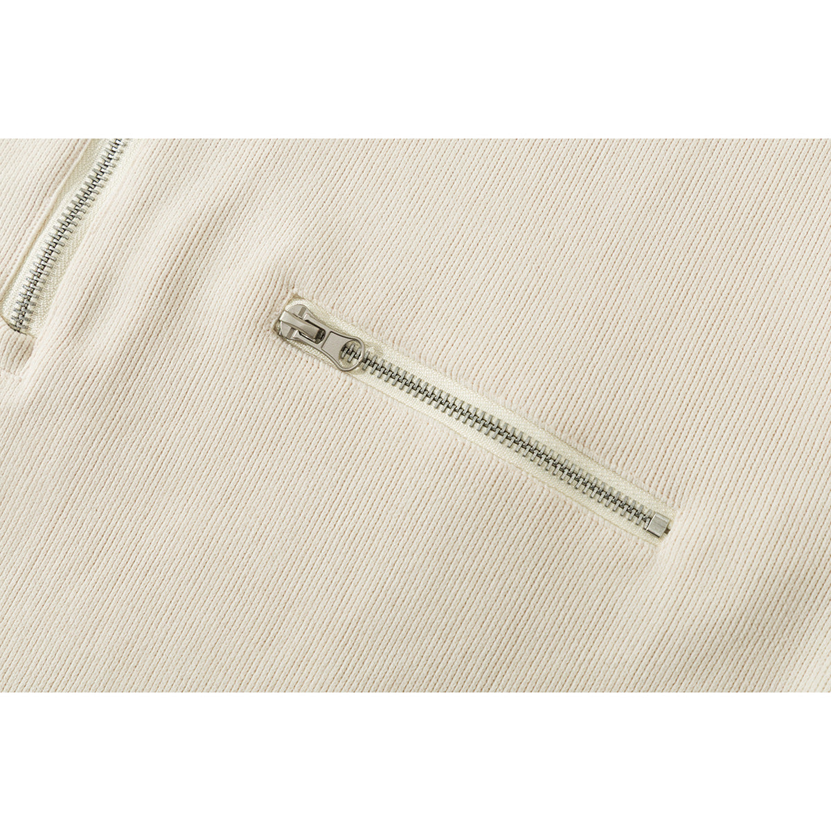 Close-up of an ivory ribbed jacket's diagonal zip pocket and metal zipper pull.