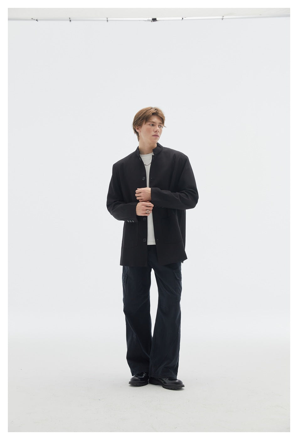 Model wearing an open black stand-collar button jacket with patch pockets, white shirt and wide black cargo pants.