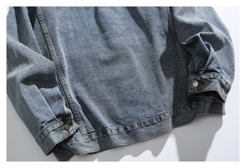 Close-up of a blue denim jacket's lower back, hem, sleeves, and buttoned cuffs laid flat.