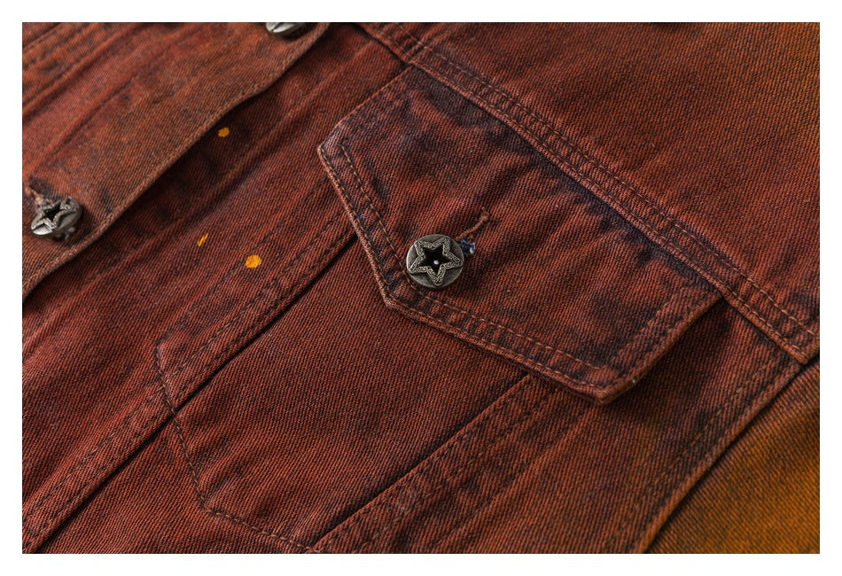 Close-up of a rust-red, dark-washed denim jacket pocket with a star-shaped metal button and contrast stitching.