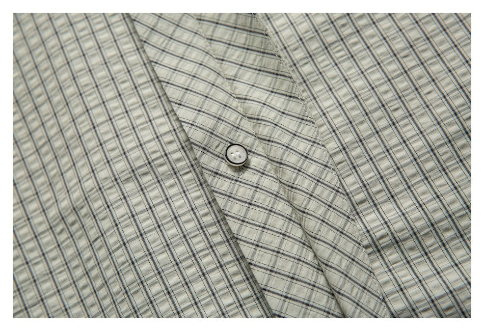 Close-up of light gray plaid fabric with intersecting dark stripes and a small white button.