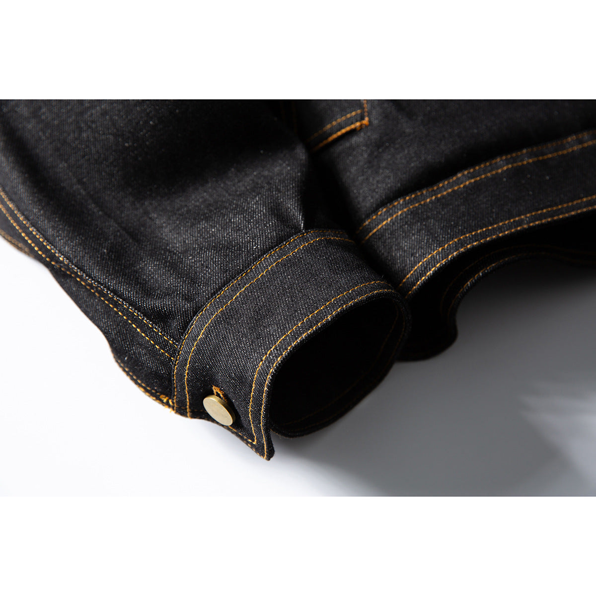 Close-up of a dark denim jacket cuff with golden contrast stitching and a brass-tone snap.