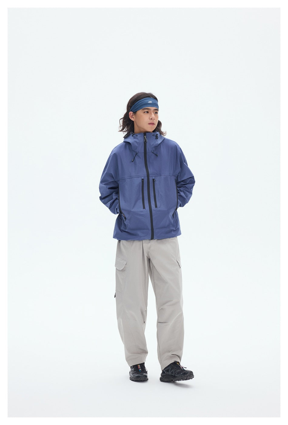Model wearing a blue hooded jacket with black zippers and light gray cargo pants, shown full length against a white