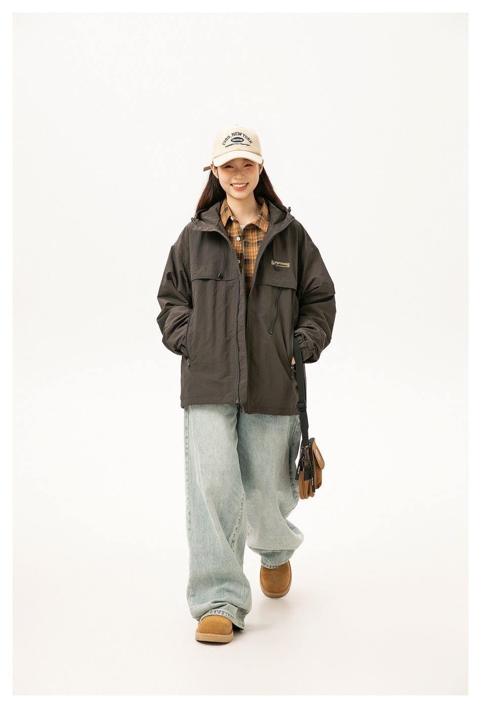 Full-length view of a woman wearing a dark brown hooded jacket over a plaid shirt and loose jeans.