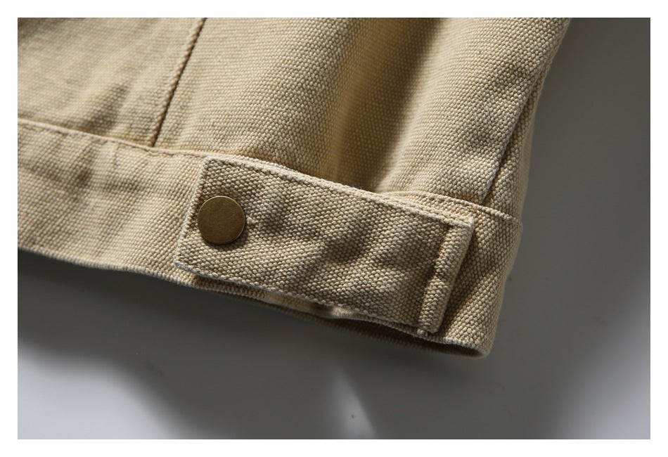 Close-up of a beige jacket hem tab with a bronze snap and visible stitching.