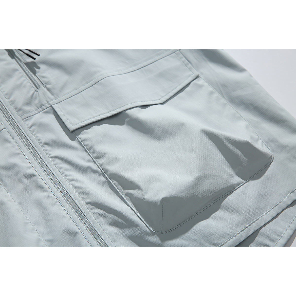 Close-up of a pale blue jacket showing its large flap pocket and central front zipper.