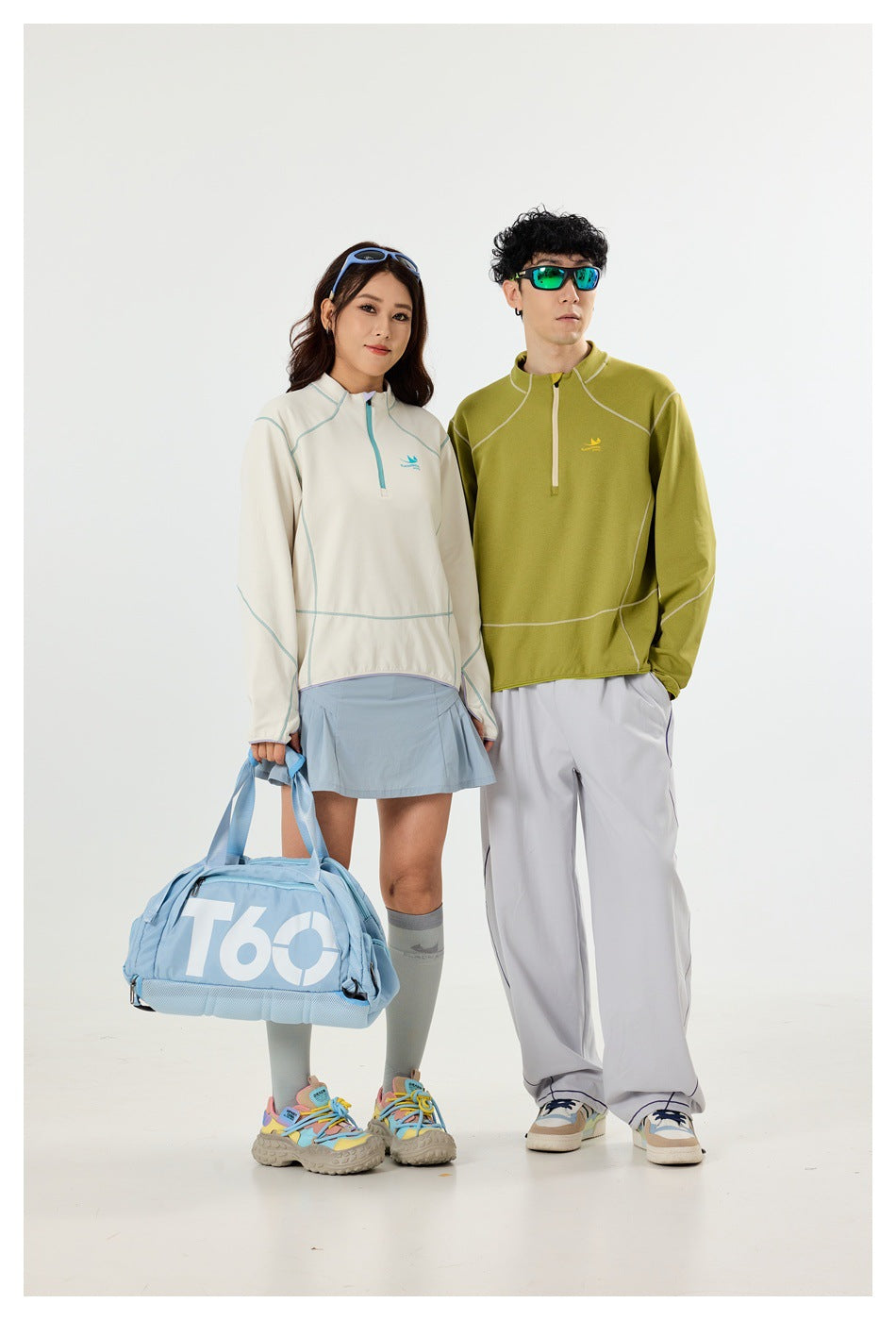 Two models wear quarter-zip pullovers: an off-white top with a pale blue skirt and an olive top with loose gray pants.