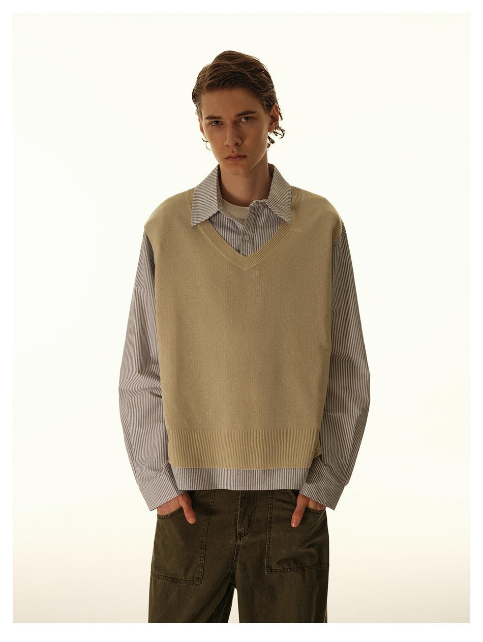 Model wearing a striped collared shirt with a tan V-neck knit vest-style panel over it, with olive pants, shown from the