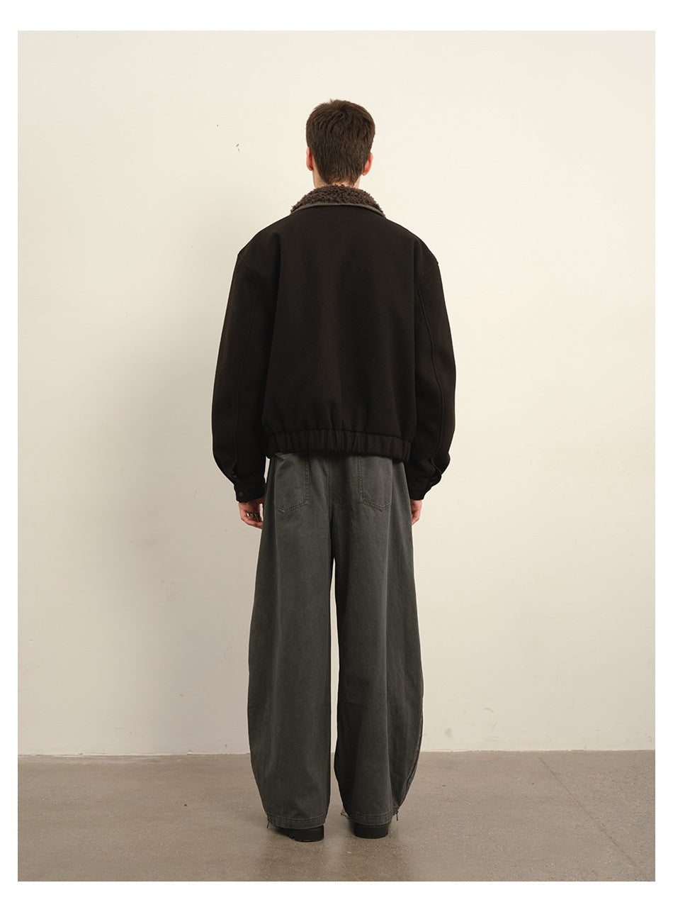 Rear view of a model wearing a black jacket with a brown textured collar and loose charcoal trousers.