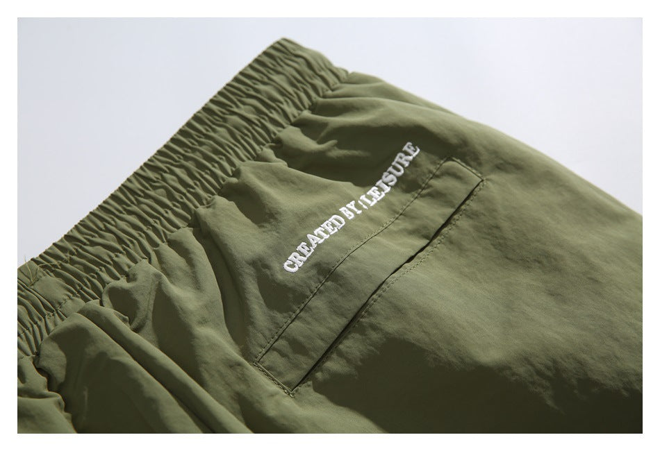 Close-up of the elastic waistband and embroidered rear pocket on olive-green shorts.