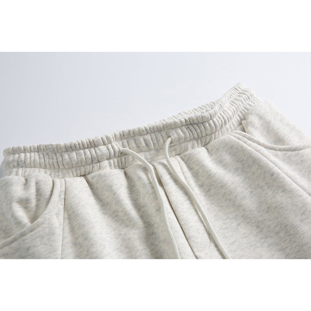 Close-up of light gray heather sweatpants showing the gathered elastic waistband, white drawstring and pocket openings.