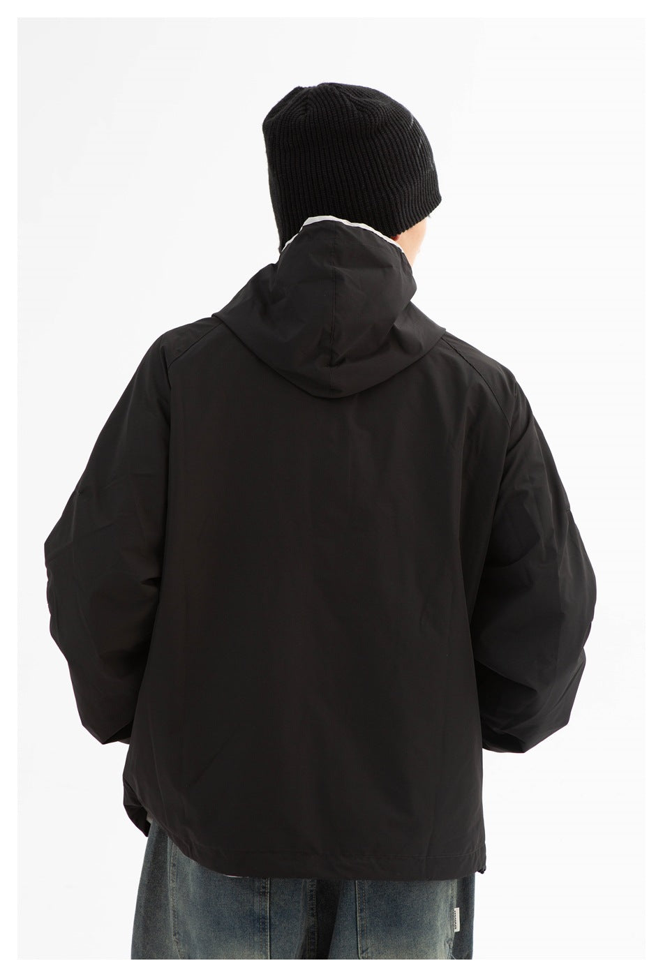 Rear view of a person wearing a black hooded jacket and black knit beanie.