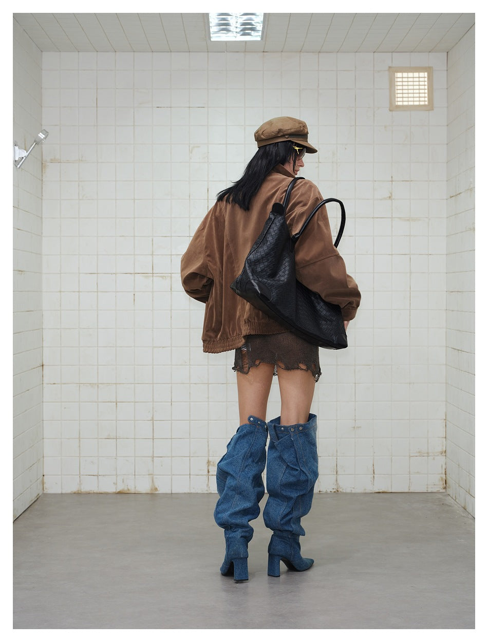 Rear view of a model in an oversized brown jacket and dark mesh mini dress, with slouchy blue denim boots.