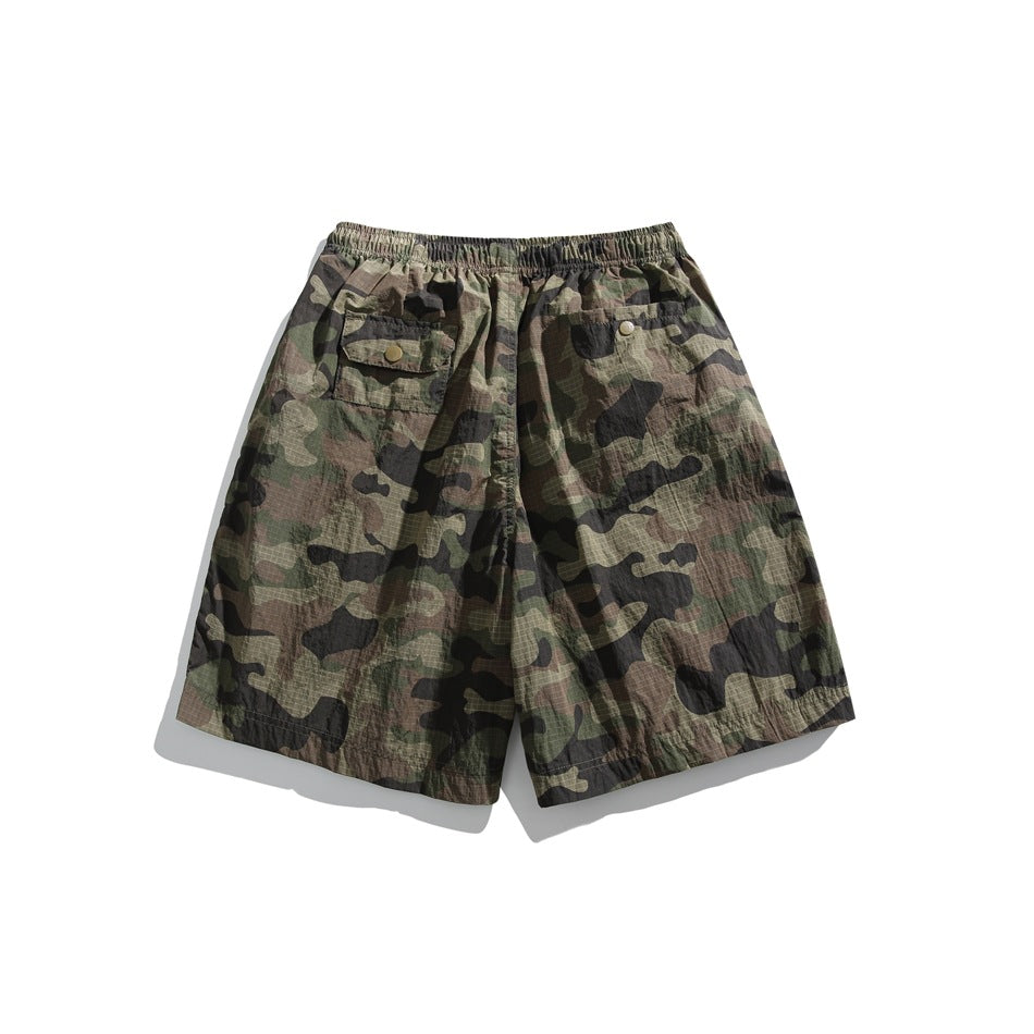 Back view of green, brown, and black camouflage shorts with an elastic waistband and two buttoned pockets.