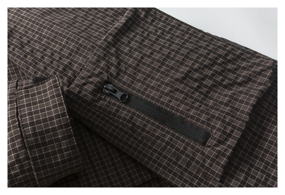 Close-up of a black zippered pocket on dark brown checked garment fabric.