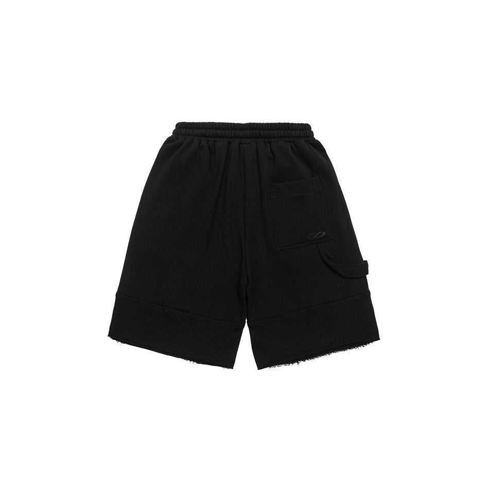 Back view of black shorts with an elastic waist, patch pocket, side strap, and raw hems.