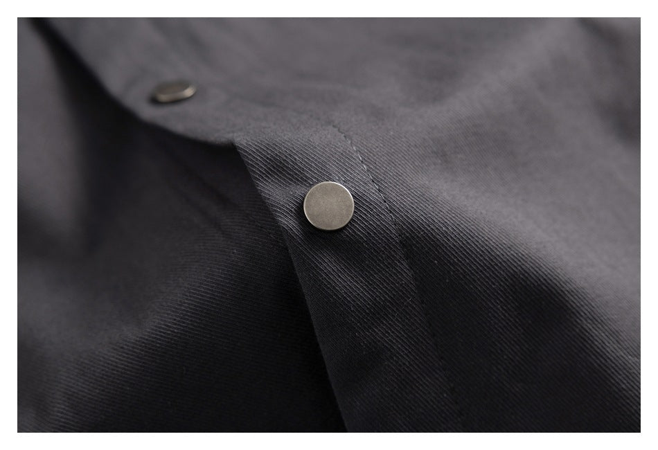 Close-up of a silver snap fastener on a stitched placket of dark charcoal fabric.
