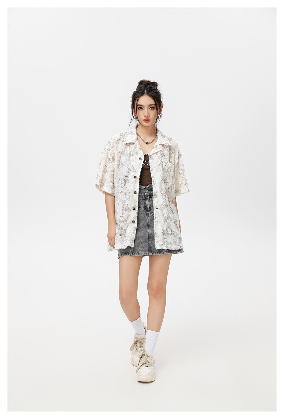 Model wearing an open white butterfly-print shirt over a dark top and gray denim mini skirt.